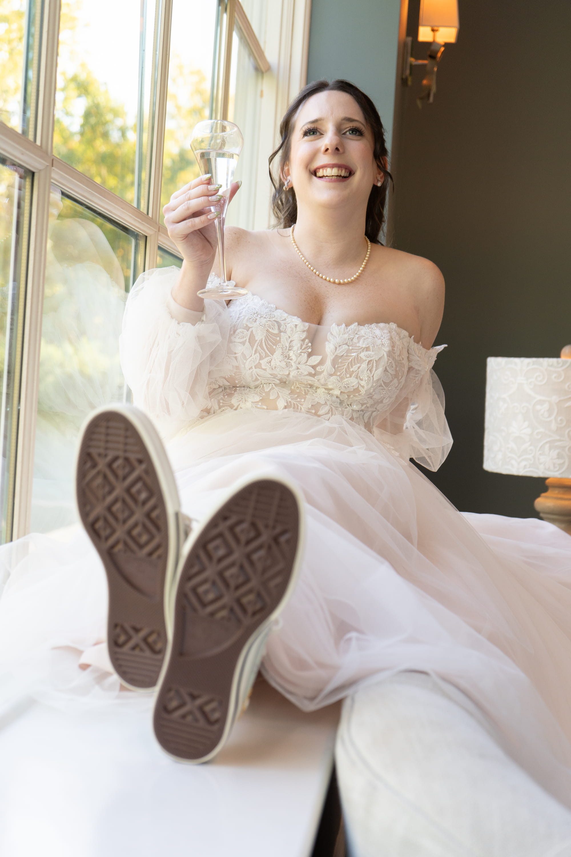 Bride laughing with champagne and Converse sneakers